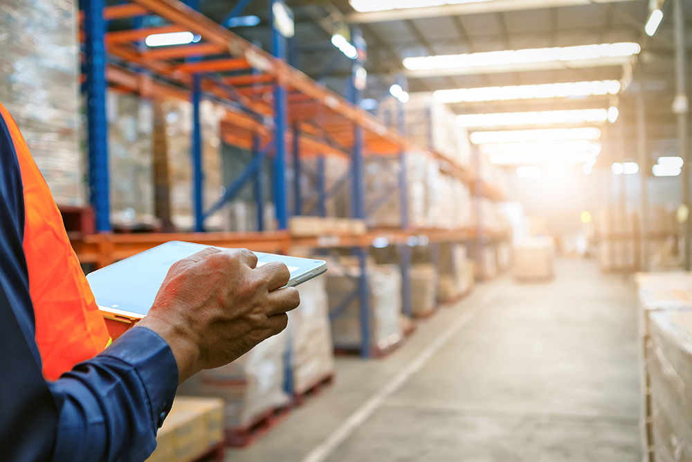 AdobeStock_435805262 man holding tablet to checking the stock products,Employee using warehouse software to checking the stock of products in the warehouse